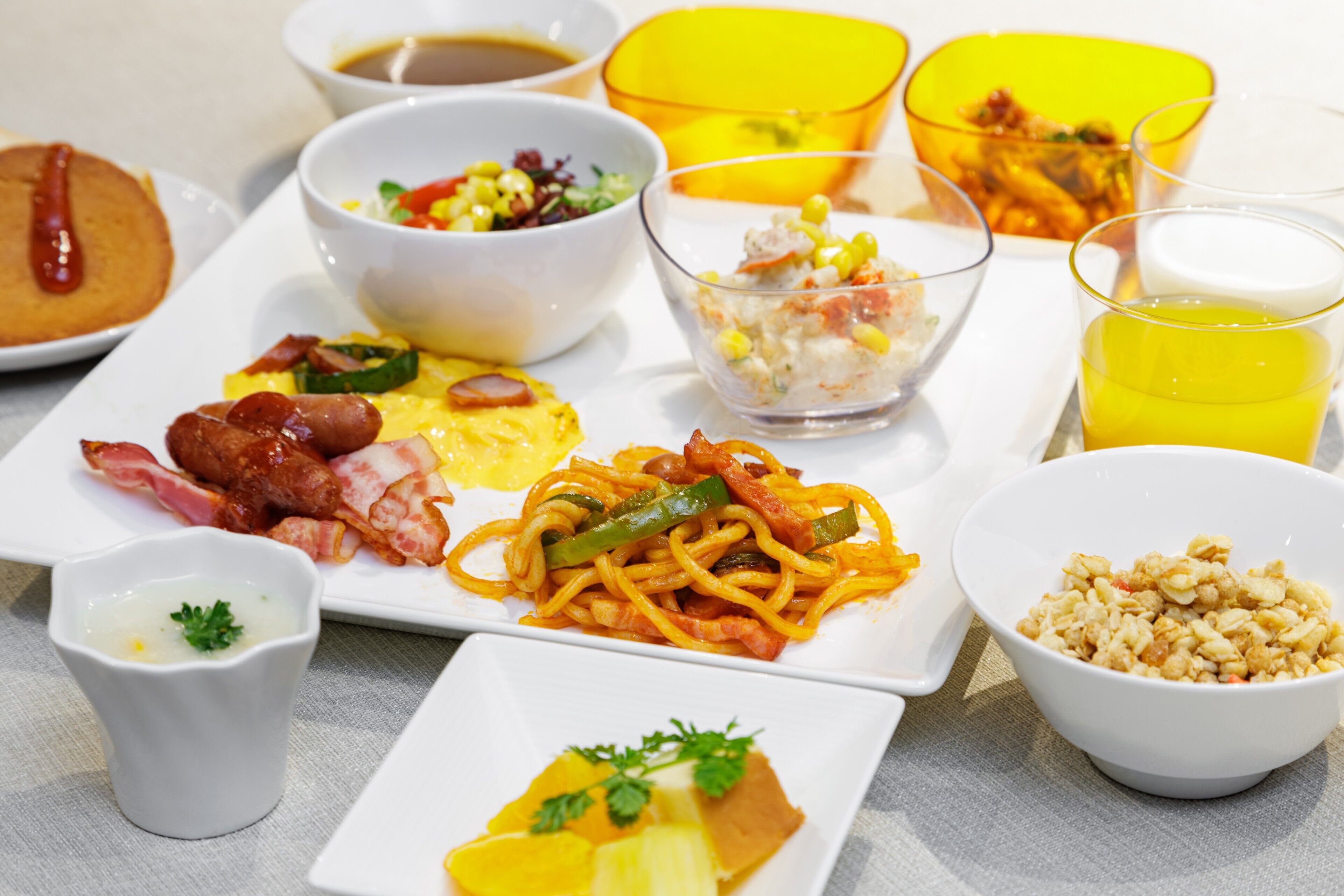 Un bufé de desayuno con diversos platos, incluyendo huevos, salchichas y una ensalada de frutas.