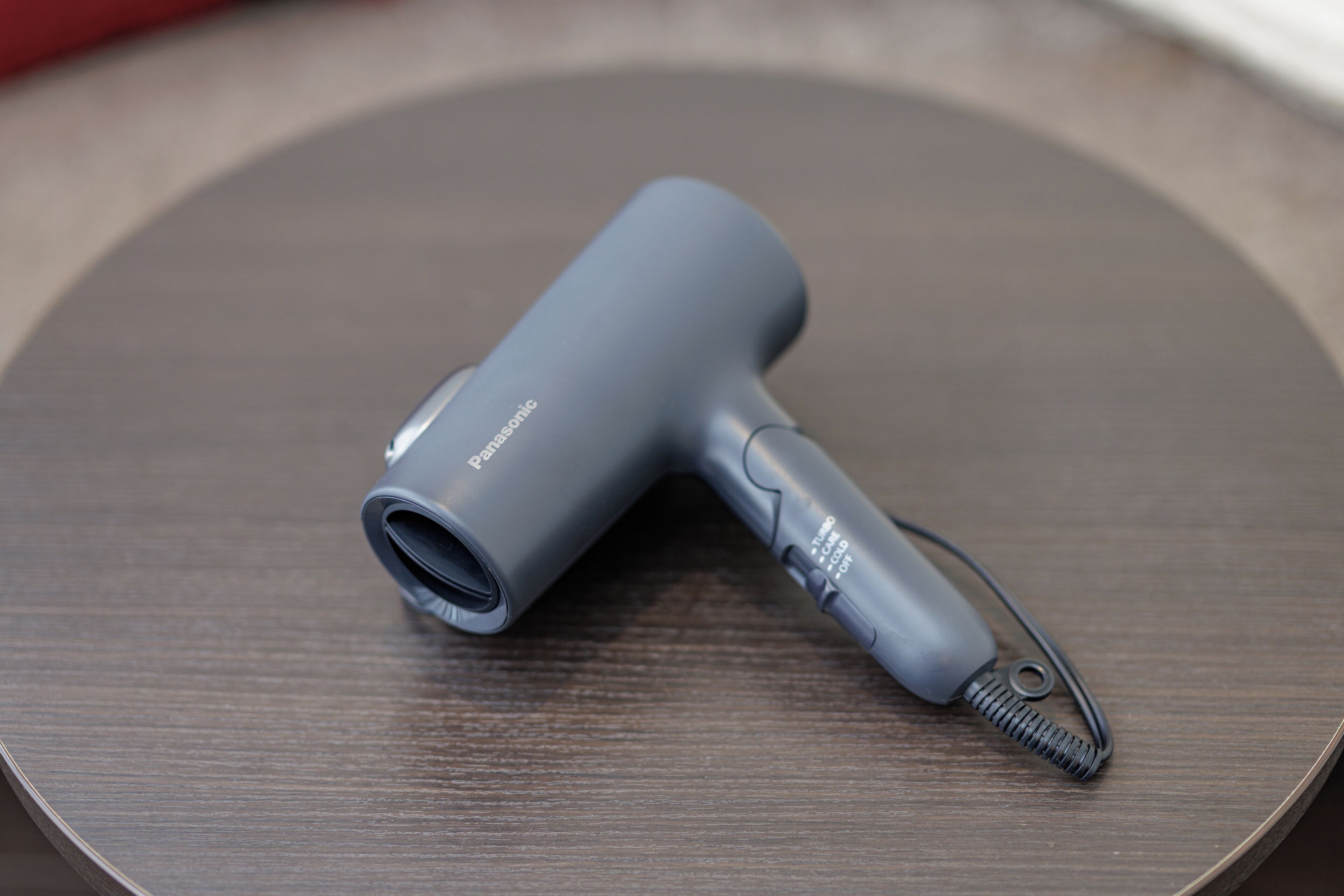 A gray hair dryer with a cord and a plug on a wooden surface.
