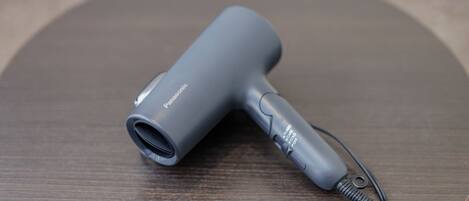 A gray hair dryer with a cord and a plug on a wooden surface.