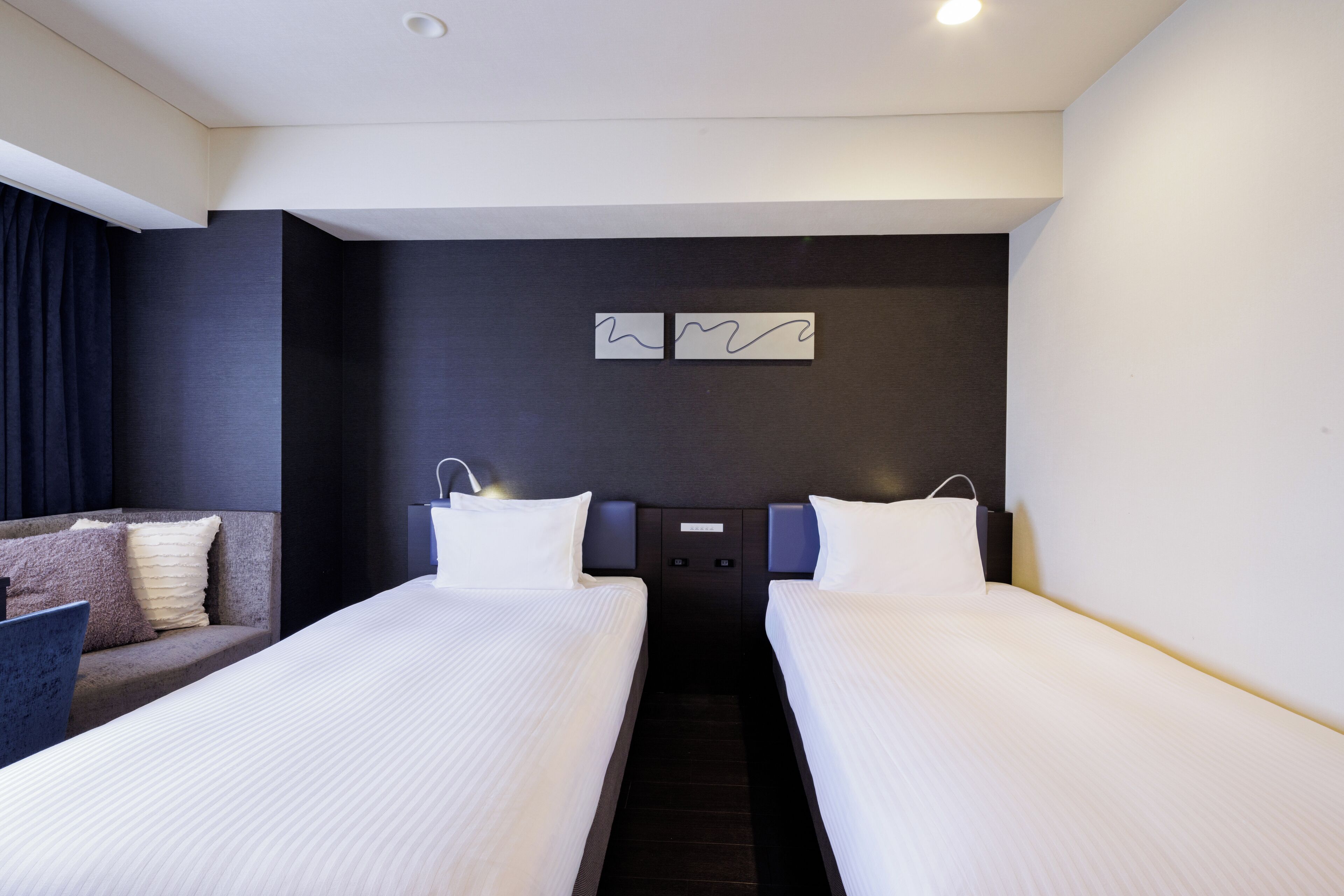Een hotelkamer met twee eenpersoonsbedden, een slaapbank en een donkere accentmuur met abstracte kunst.