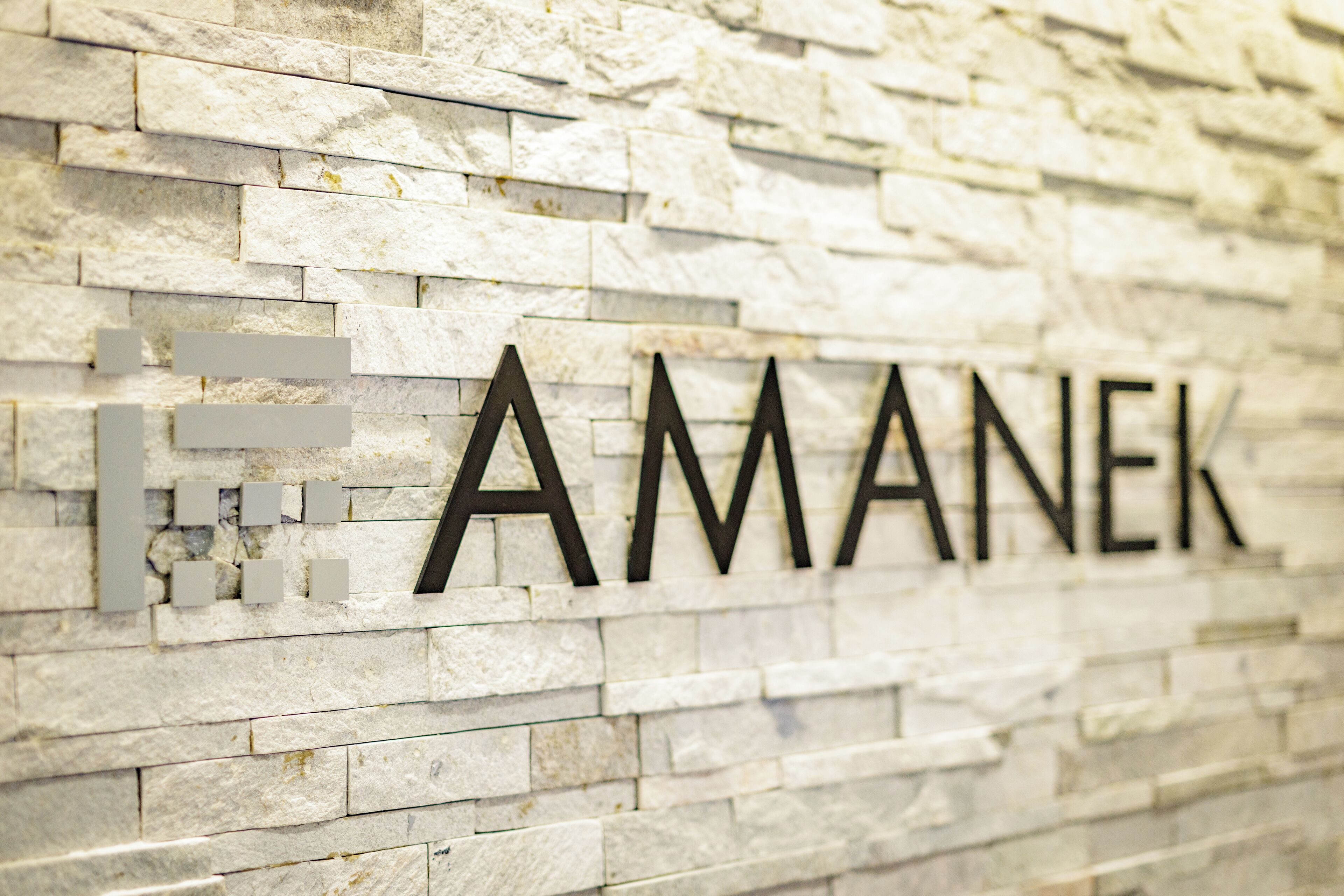 Un muro di pietra con la scritta "AMANEK" in grandi caratteri.