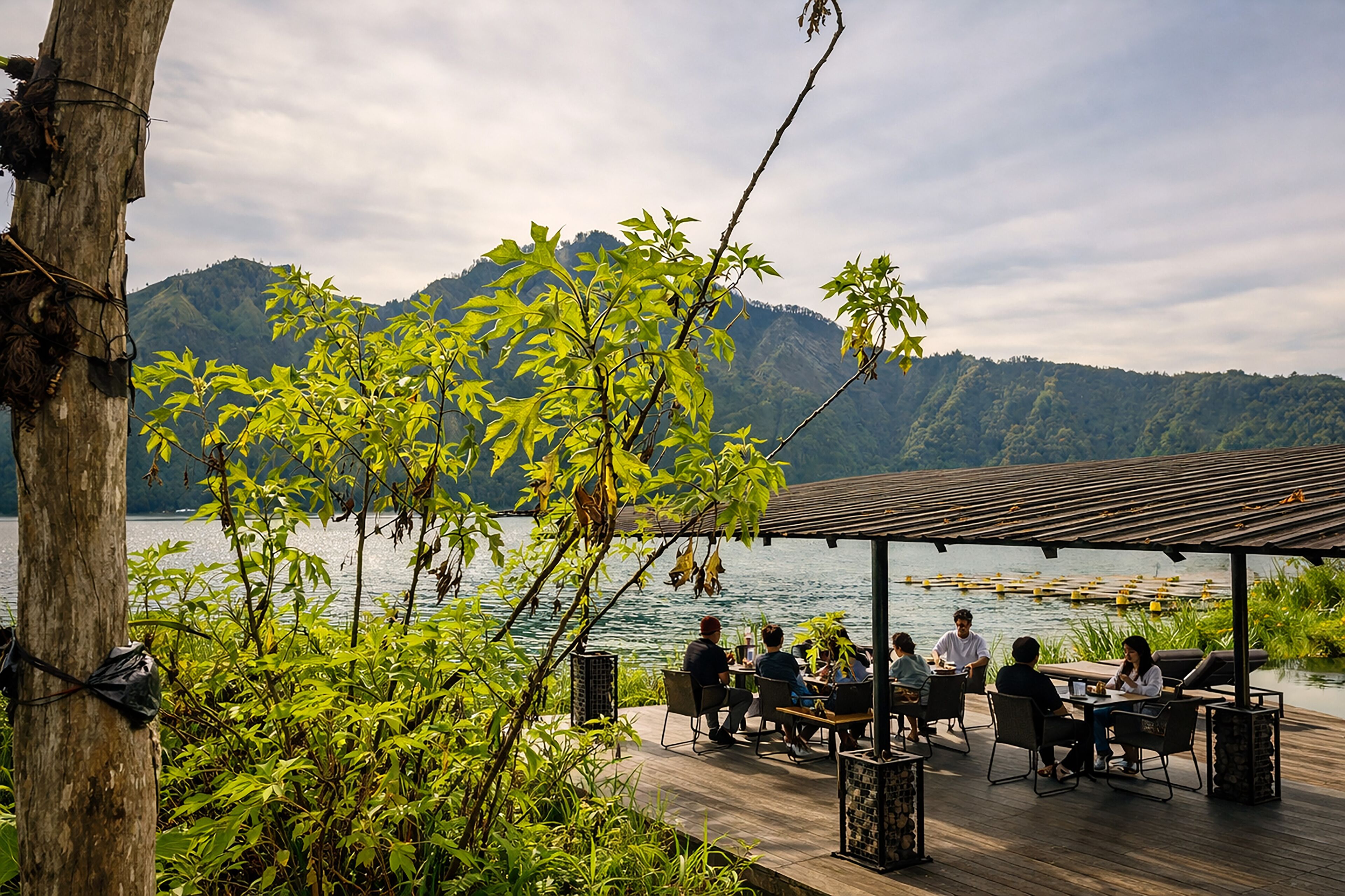 An outdoor dining area with tables and chairs, overlooking a body of water and hills.