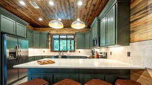 A modern kitchen with a large island, green cabinets, and wooden ceiling beams. - Sleeps 18 people with a private heated pool, hot tub, playground, fire pit, and a private arcade! (Broken Bow)