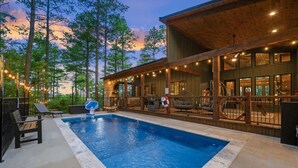 A swimming pool with a lifeguard chair and lounge chairs, surrounded by wooden deck and string lights. - Sleeps 18 people with a private heated pool, hot tub, playground, fire pit, and a private arcade! (Broken Bow)