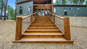 A wooden staircase leading to a building with a stone wall and a wooden deck. - Sleeps 18 people with a private heated pool, hot tub, playground, fire pit, and a private arcade! (Broken Bow)