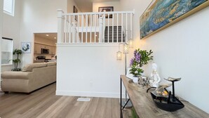 Un vaste espace de vie doté d’un haut plafond, d’un plancher en bois, d’un escalier blanc, d’une table à manger agrémentée d’objets décoratifs et d’un grand tableau abstrait accroché au mur.
