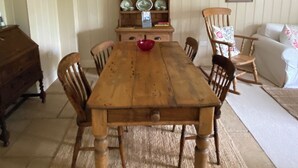 Un comedor con una mesa de madera, seis sillas, un armario de madera con vajilla y un sofá blanco.