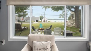 A room with a large window overlooking a grassy area with outdoor furniture and a stone wall.