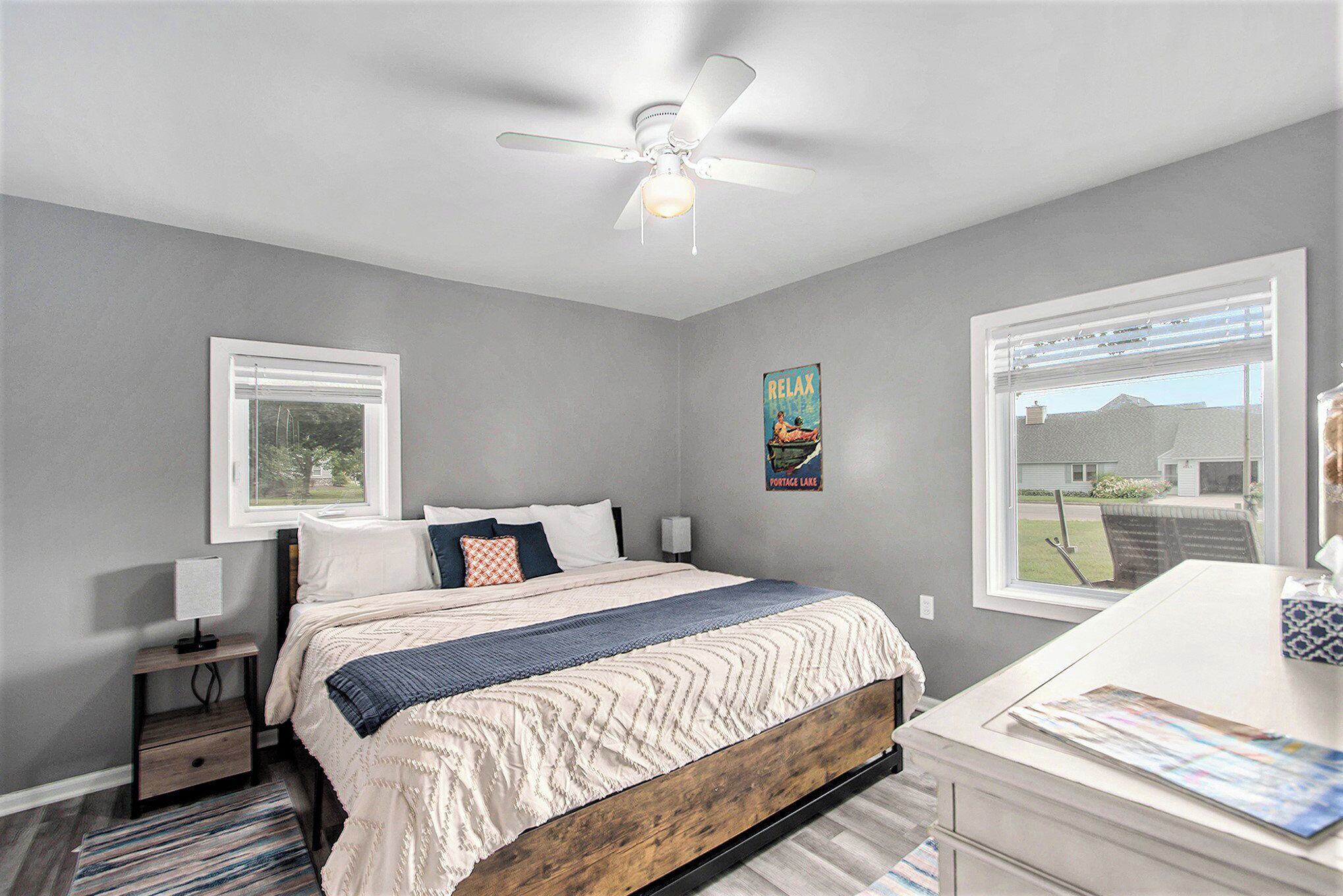 A bedroom with a bed, a nightstand, a desk, a ceiling fan, and a poster on the wall.