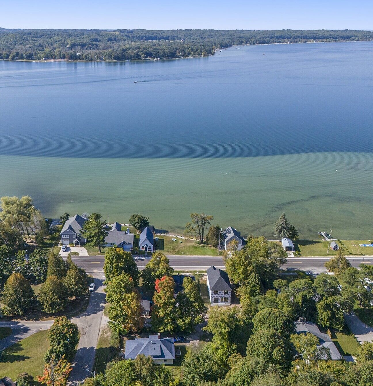 A residential area with houses and a road, surrounded by trees and a large body of water.
