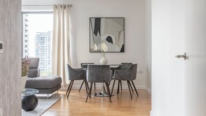 Un salon moderne avec un canapé gris, une table à manger et quatre chaises, ainsi qu’un grand tableau abstrait accroché au mur.