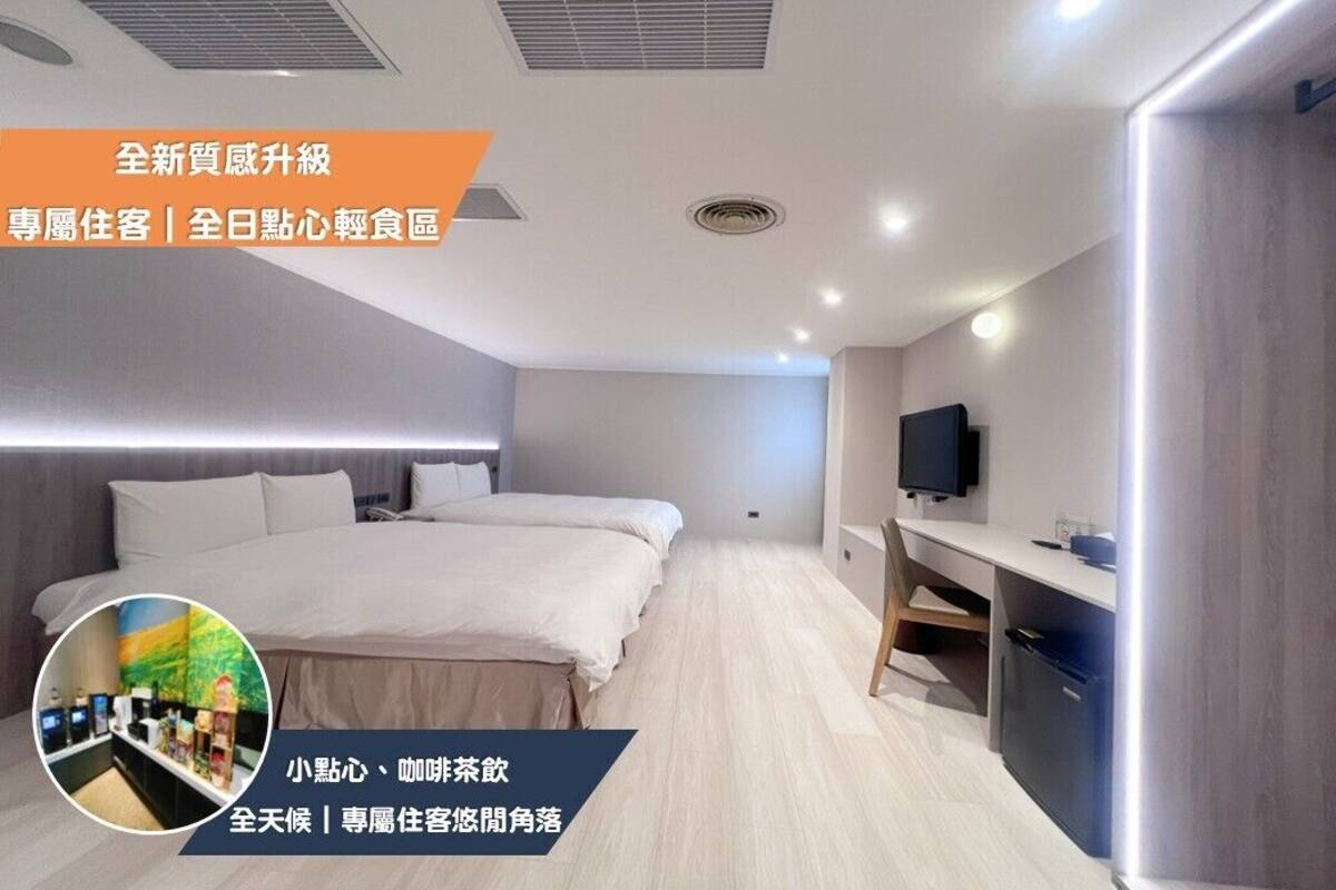 Ein modernes Hotelzimmer mit einem großen Bett, einem Schreibtisch und einem Fernseher. Es gibt eine kleine Küchenzeile mit einem Kühlschrank und einer Mikrowelle.