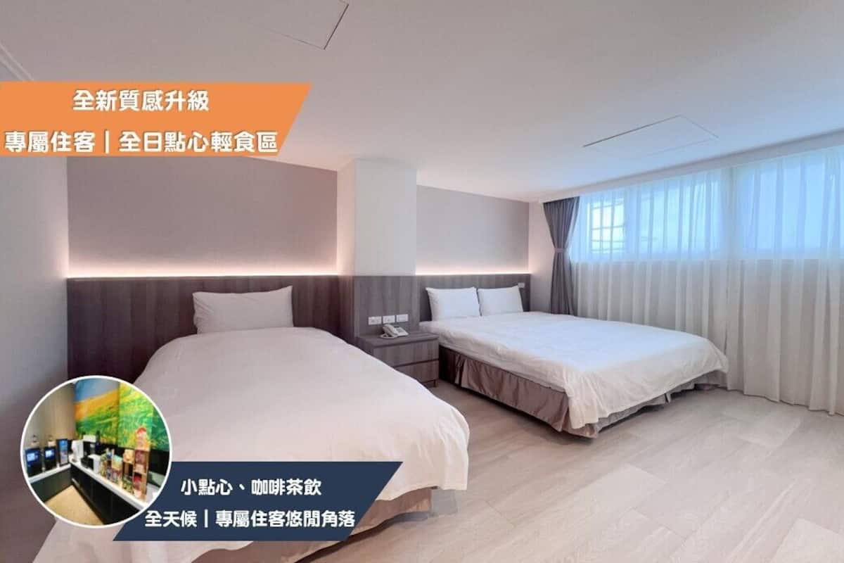 Ein modernes Hotelzimmer mit zwei Betten, einem kleinen Schreibtisch und einem großen Fenster mit Vorhängen.