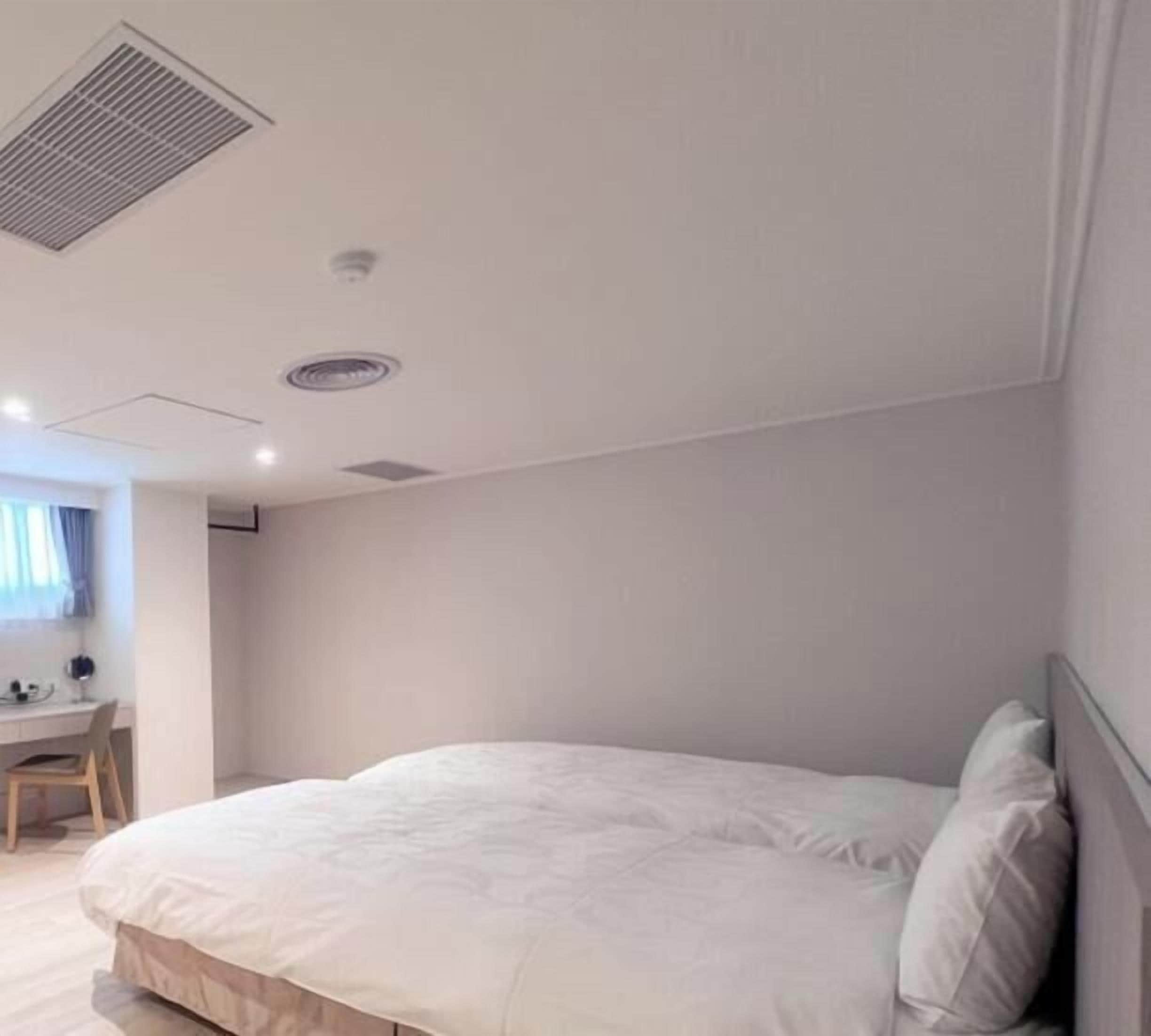 A hotel room with a large bed, a desk with a computer, and a small kitchenette.