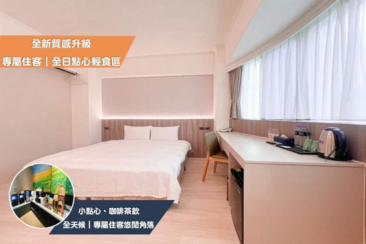 Ein Hotelzimmer mit Bett, Schreibtisch und Fenster. Es gibt eine kleine Küchenzeile mit einer Mikrowelle und einem Wasserkocher.