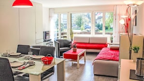 Un salón moderno con una mesa de comedor de vidrio, sofás grises y una pared de acento roja.
