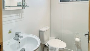 Une salle de bain avec un lavabo blanc, des toilettes et une fenêtre située au-dessus des toilettes.