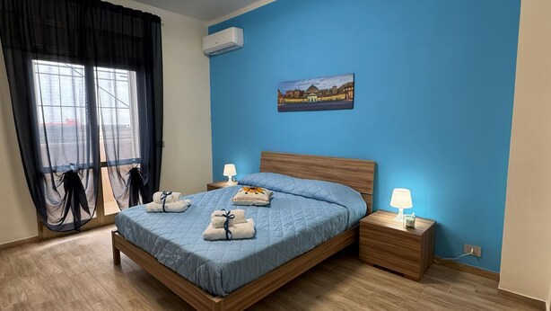 Une chambre moderne avec un lit en bois, un bureau avec une chaise et une vue sur le paysage urbain par la fenêtre.