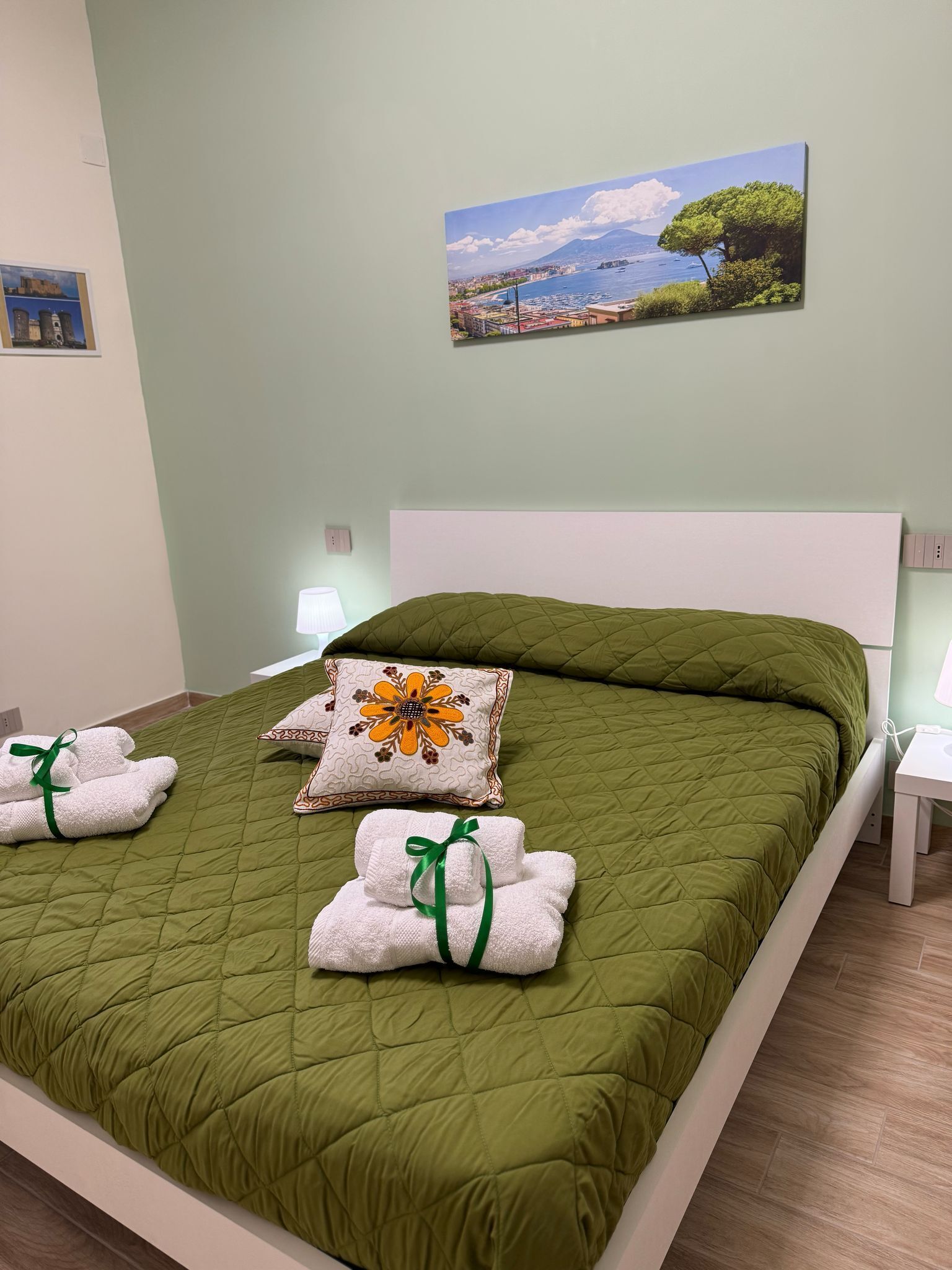 Ein ordentlich gemachtes Bett mit einer grünen Decke, zwei Kissen und Handtüchern mit grünen Bändern.