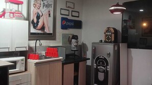 A compact kitchen with a microwave, coffee machine, and refrigerator. There is a red stool and a framed poster on the wall. - FreeStayle Home (Callao)
