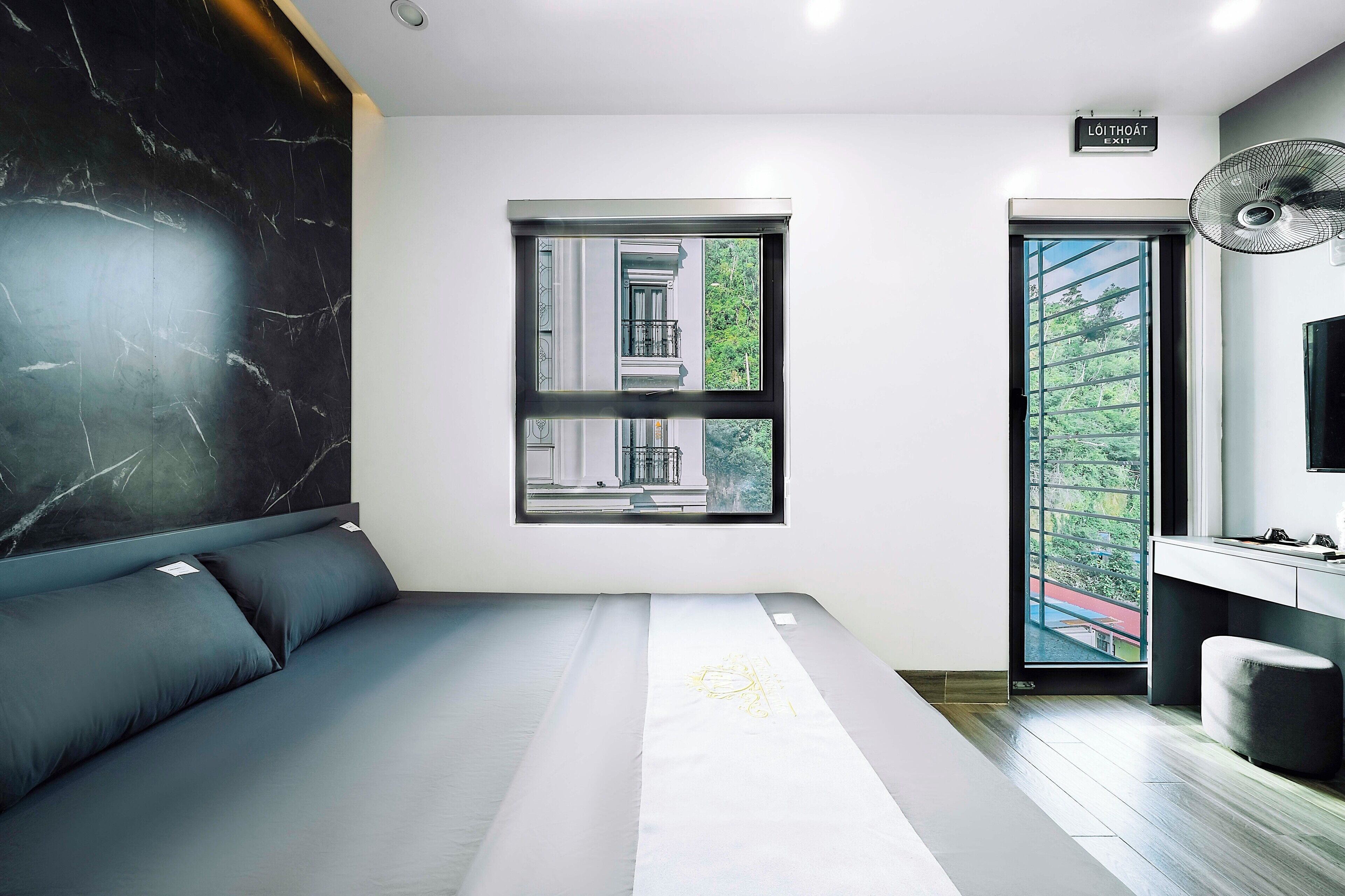 Een moderne slaapkamer met een groot bed, een raam met uitzicht op groen en een klein bureau.