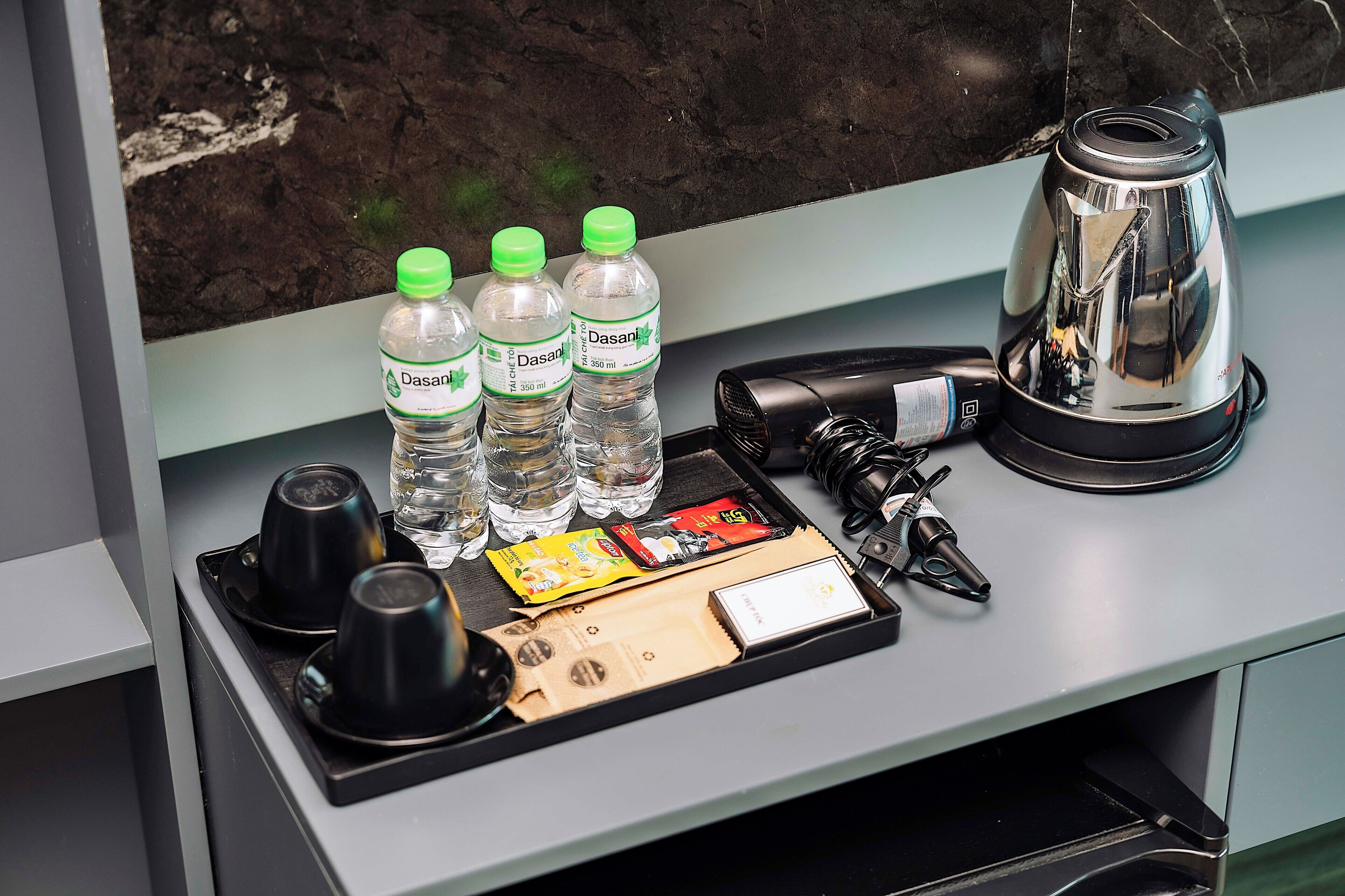 A tray with water bottles, a coffee maker, a camera, and some snacks on a counter.