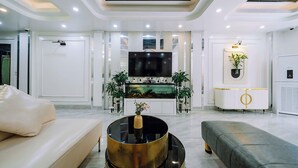 A modern living room with a flat-screen TV, a round gold coffee table, and a grey sofa. - Cat Ba Nam Phong Hotel (Hai Phong)