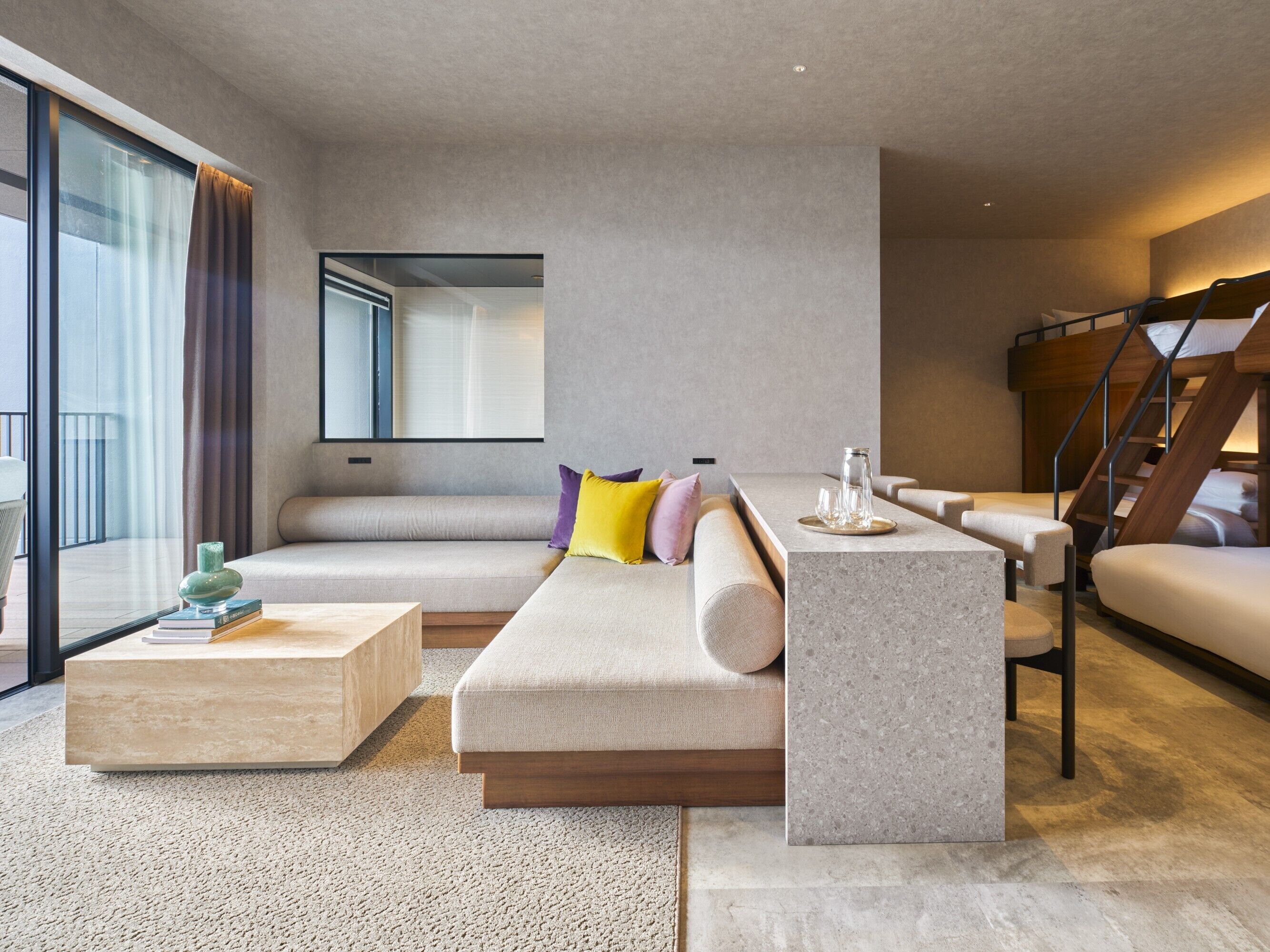 Een moderne woonkamer met een bank, een salontafel, een klein keukentje en een trap.