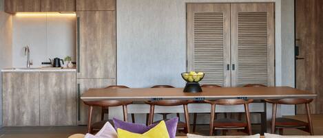 A modern kitchen with wooden cabinets, a dining table with chairs, and a sofa with cushions.