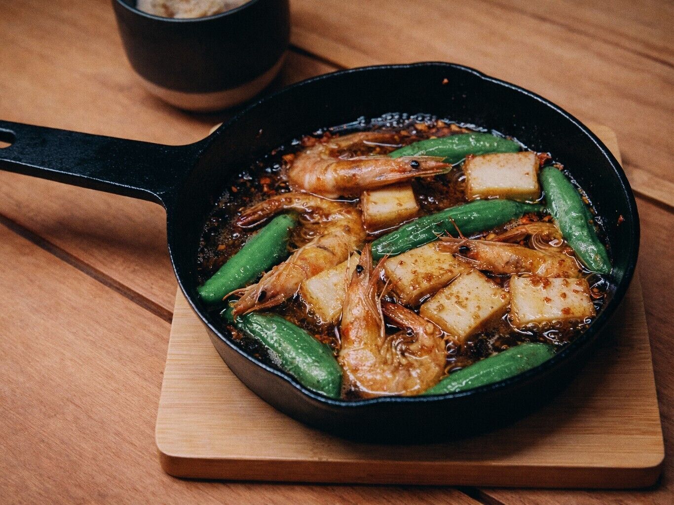 Une poêle contenant des crevettes et des légumes verts, le tout posé sur une planche en bois.