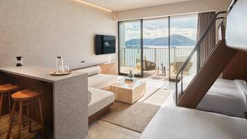 A modern hotel room with a balcony, a flat-screen TV, a kitchen area, and a large bed.