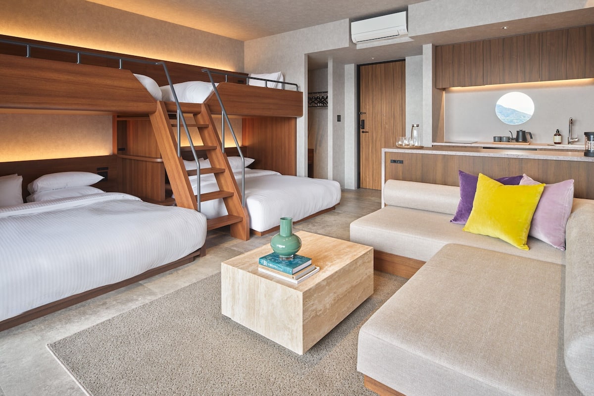 A modern hotel room with bunk beds, a sofa, a coffee table, and a kitchen area.
