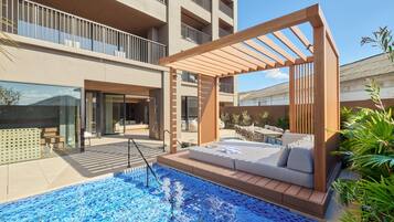 A modern outdoor pool area with a wooden pergola, seating, and a view of a high-rise building.