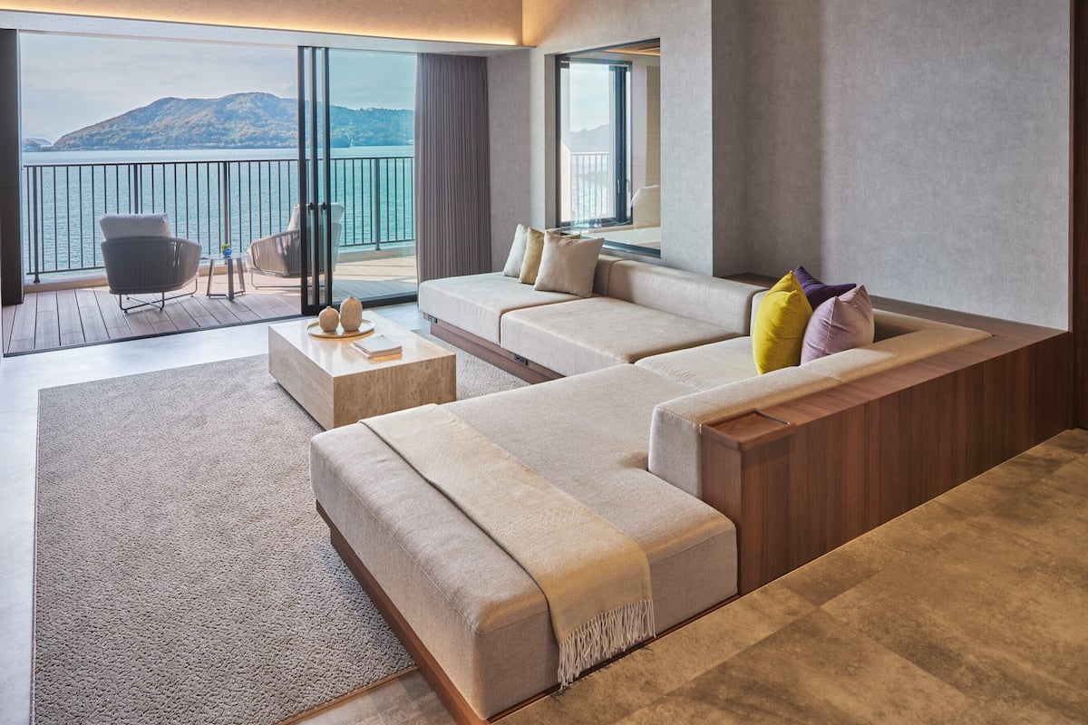 A modern living room with a large sofa, a coffee table, and a view of the sea through a balcony.