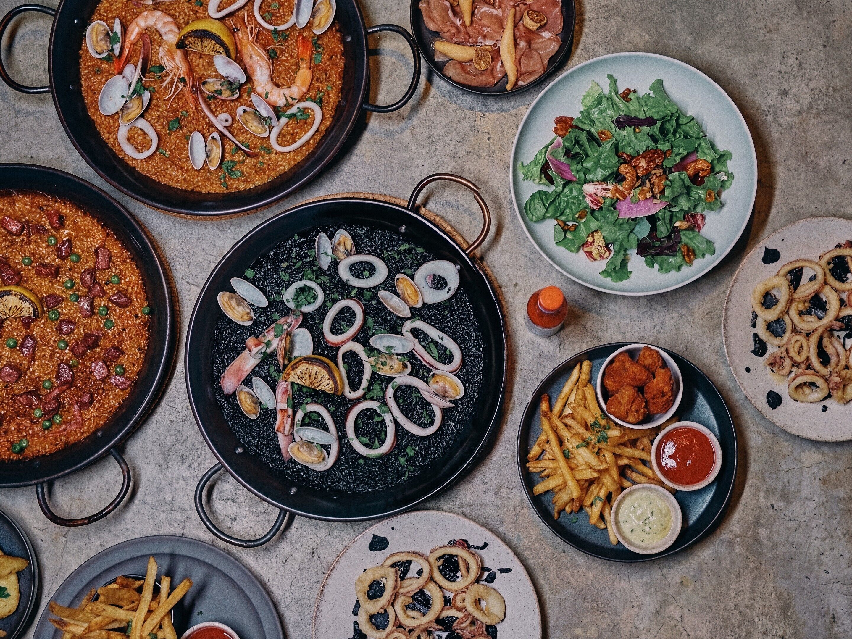 A variety of dishes including seafood paella, fries, and salads.