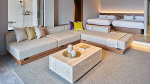 Une chambre d’hôtel moderne dotée d’un grand canapé en forme de L, d’un lit séparé, d’une petite table basse et d’un grand miroir.