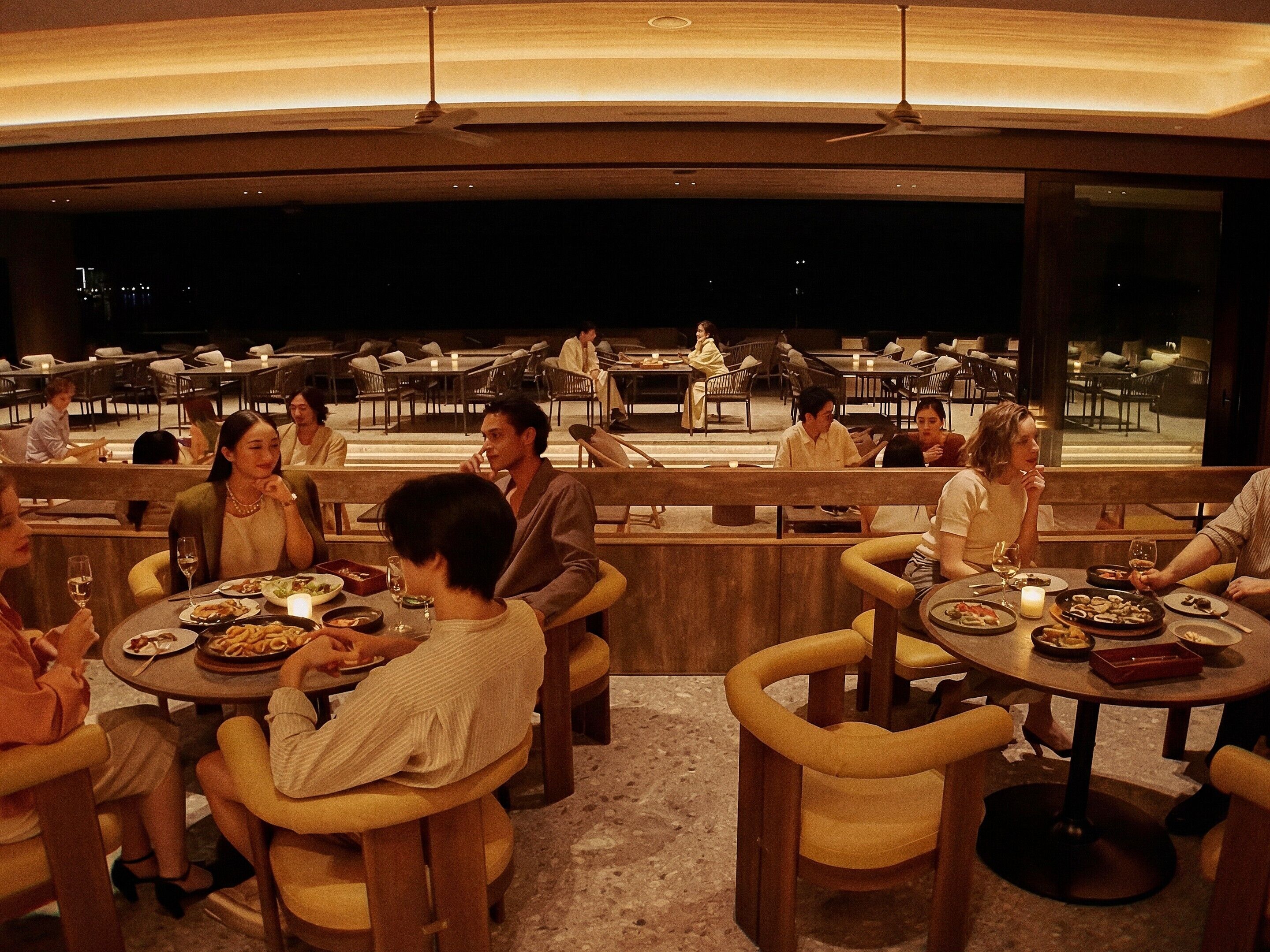 A restaurant with round tables and chairs, a view of the city at night, and a modern interior design.