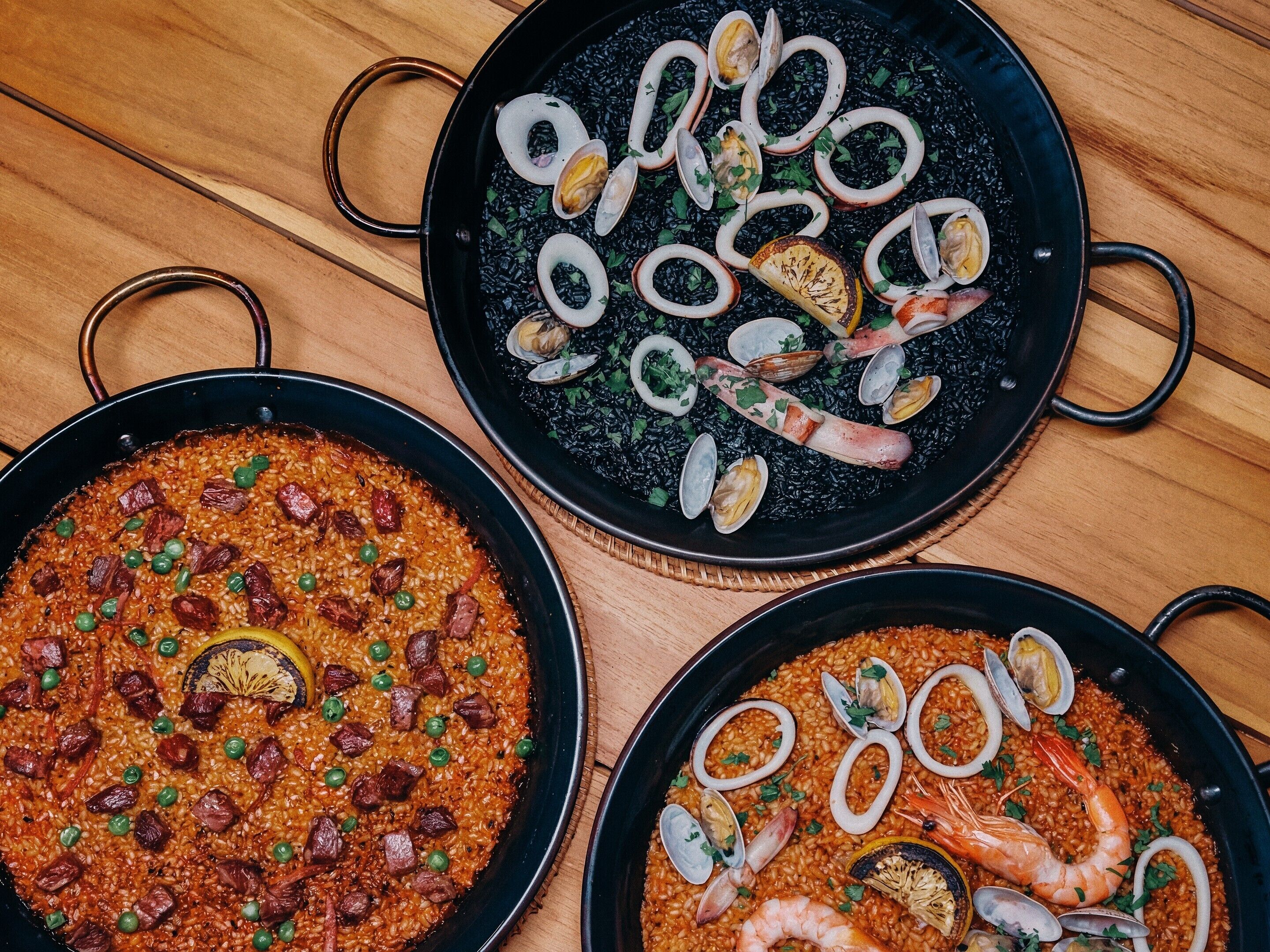 Tres paellas grandes de mariscos sobre una mesa de madera.