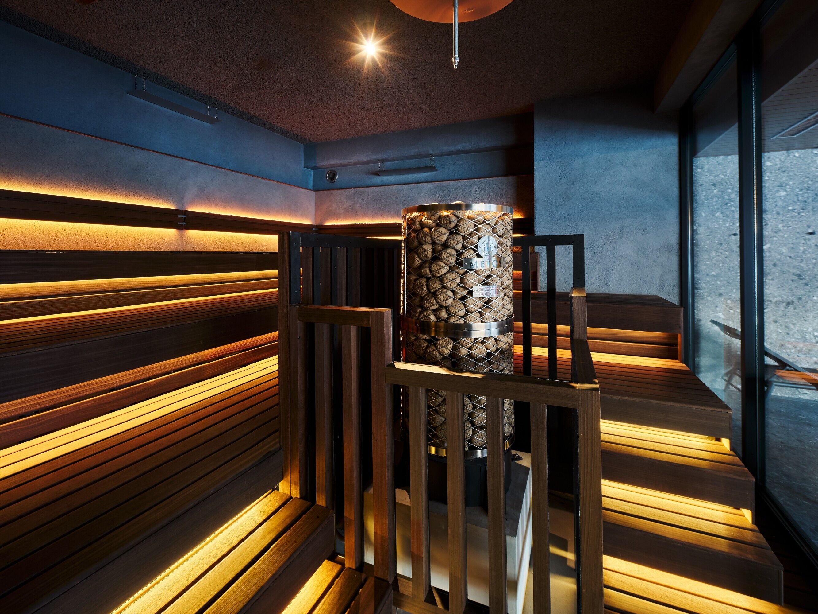 Una sauna moderna con bancos de madera y un calentador cilíndrico central.
