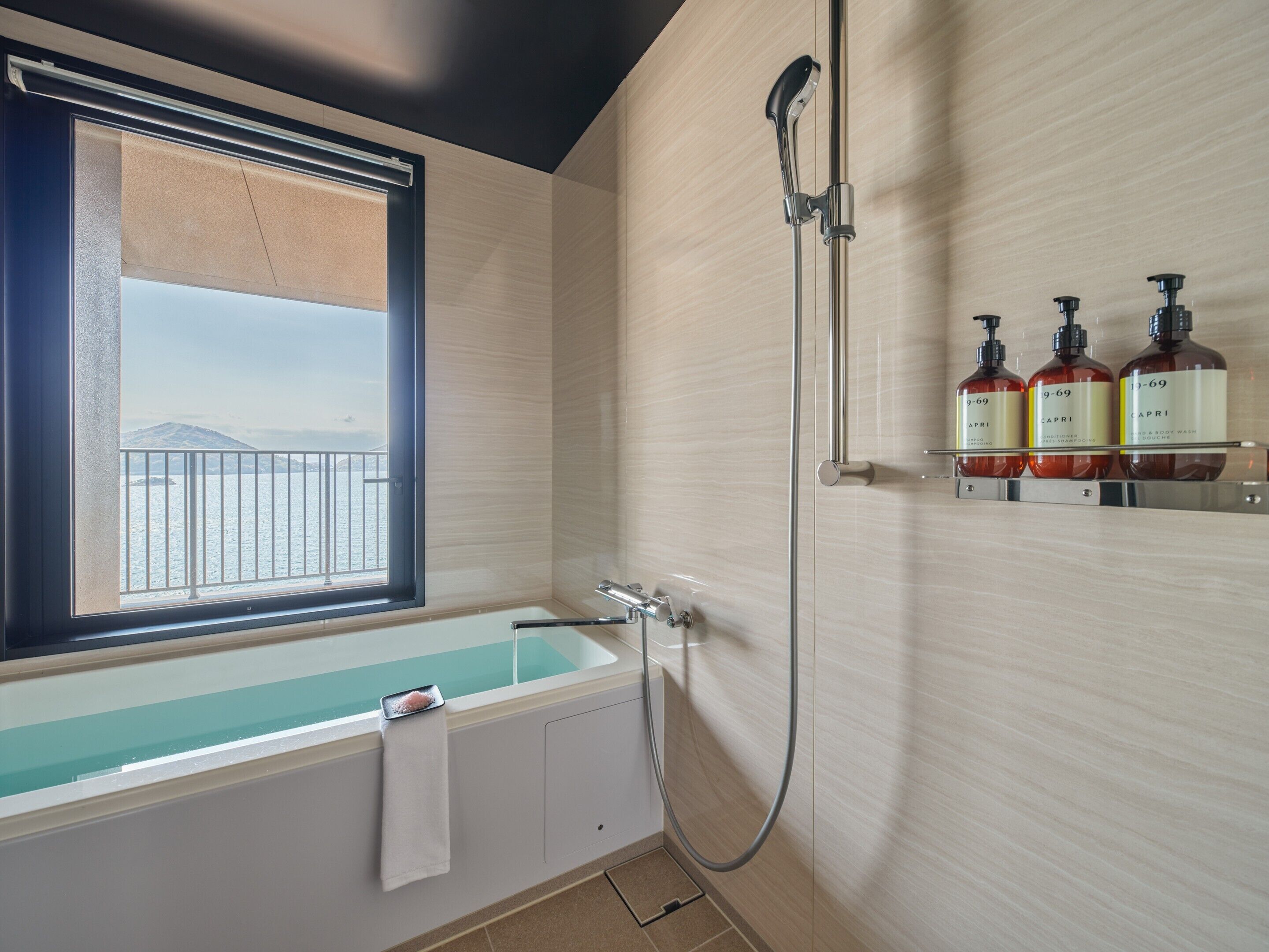Une salle de bain équipée d’une baignoire, d’une douche et d’une fenêtre donnant sur un plan d’eau.