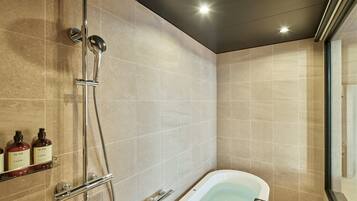 A modern bathroom with a freestanding bathtub, a handheld showerhead, and two bottles of hand soap on a shelf.