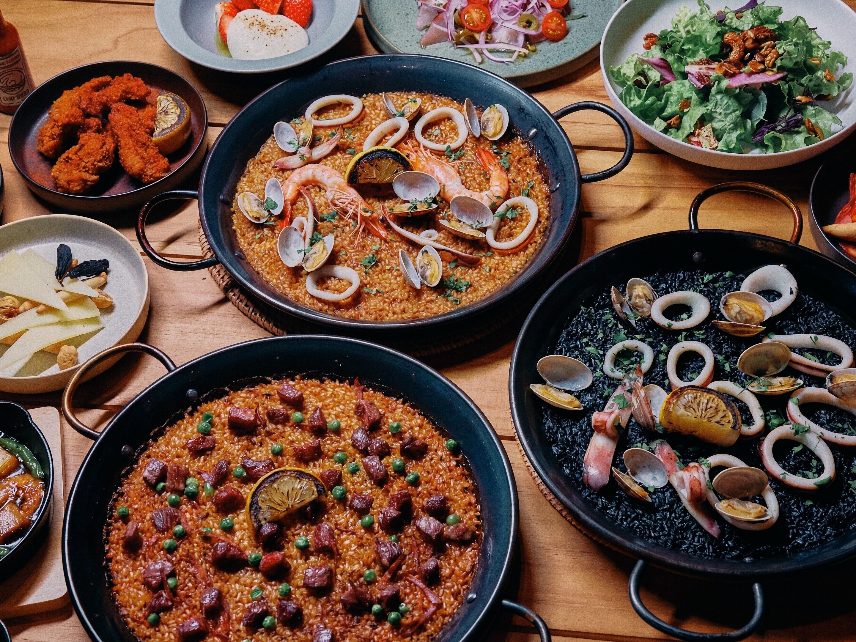A variety of dishes including seafood paella, a salad, and other meals on a wooden table.