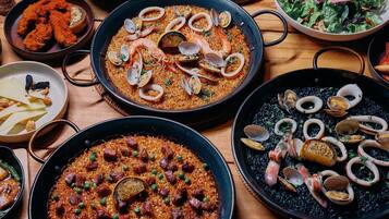A variety of dishes including seafood paella, a salad, and other meals on a wooden table.