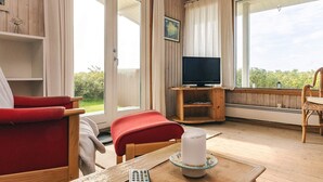 A cozy room with a wooden floor, a red chair, a television on a wooden stand, and a large window with curtains. - 6 Person Holiday Home in Lundby (Lundby)