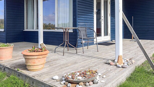 A blue house with a porch, a table, a chair, and potted plants. - 6 Person Holiday Home in Lundby (Lundby)