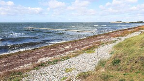 A coastal landscape with a rocky shoreline, a wooden pier extending into the sea, and a grassy area beside the path. - 6 Person Holiday Home in Lundby (Lundby)