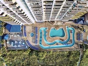 A high-rise hotel with a rooftop pool, sun loungers, and a tennis court.