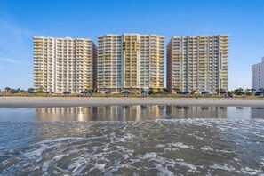 A beachfront hotel with multiple high-rise buildings, a sandy beach, and umbrellas.