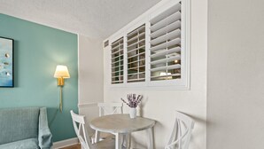 Un coin repas avec une table ronde, des chaises blanches, un mur de couleur turquoise et une fenêtre avec des volets.