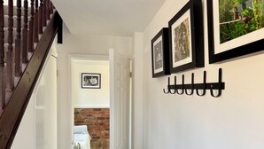 Um corredor com escada de madeira, porta-roupas e quadros nas paredes.